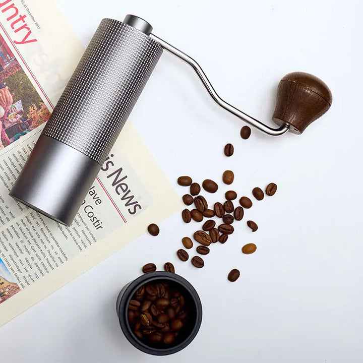 Silver manual coffee grinder with coffee beans on a newspaper flat lay